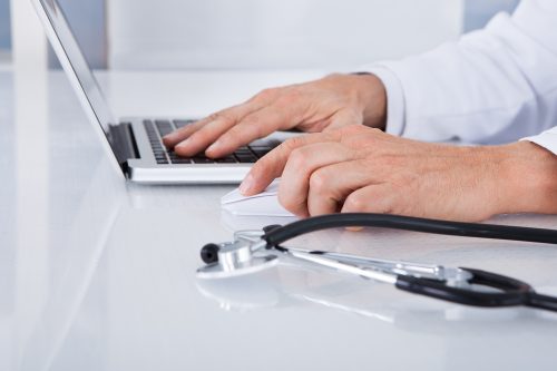 Image of the hands on a keyboard, with a stethescope nearby. A health professional using computer